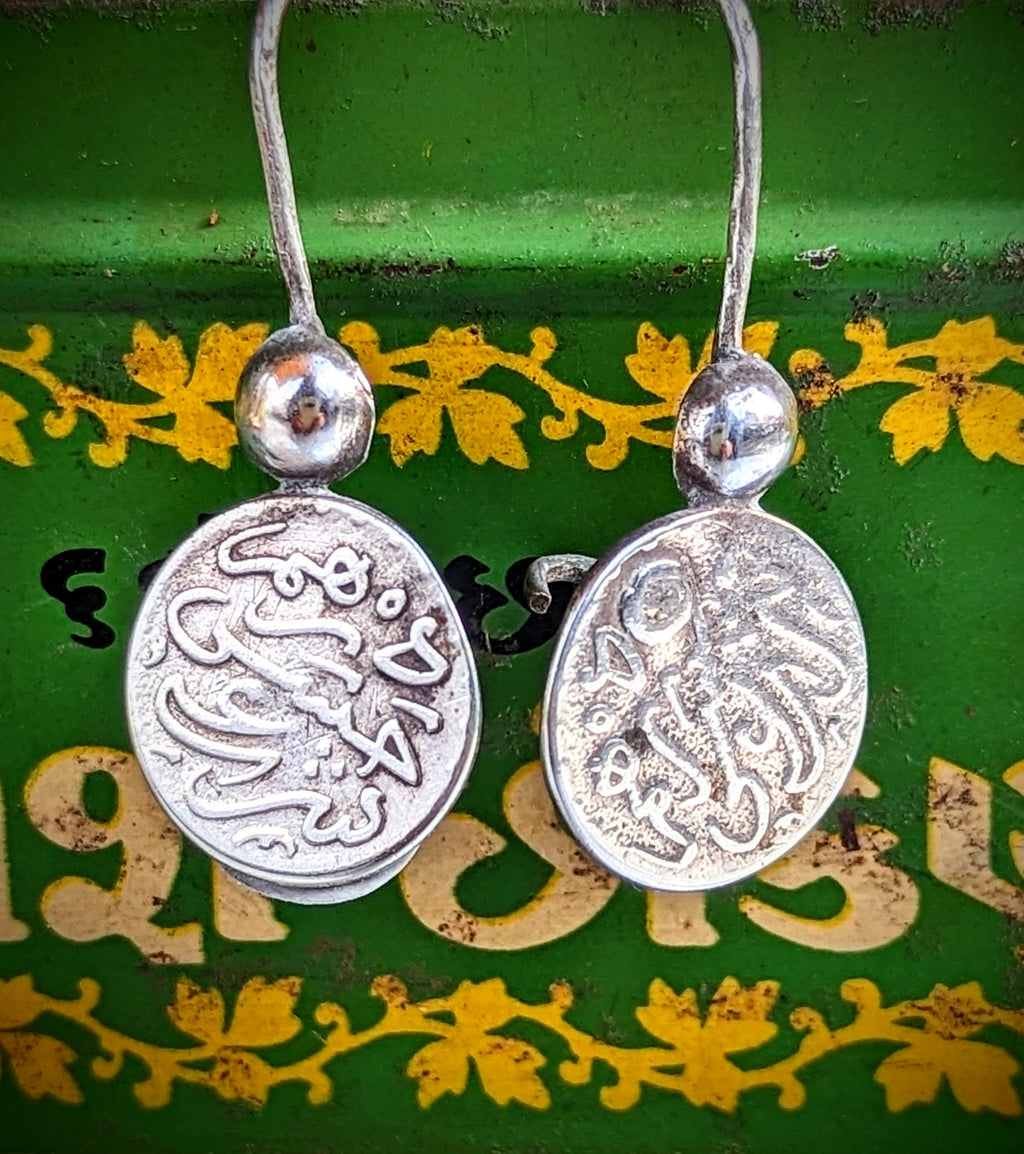 Handmade antique silver Amazigh coin earrings. These are from the Southern Atlas mountains .We love the little hands that are holding the coins!!

These are original pieces so the earring wires are slightly thicker than modern earrings.

Tribal antique silver traditionally has no hallmarks, but all that we sell have an 80-90% content, as these pieces would have been historically made from old melted down jewellery and coins.   
