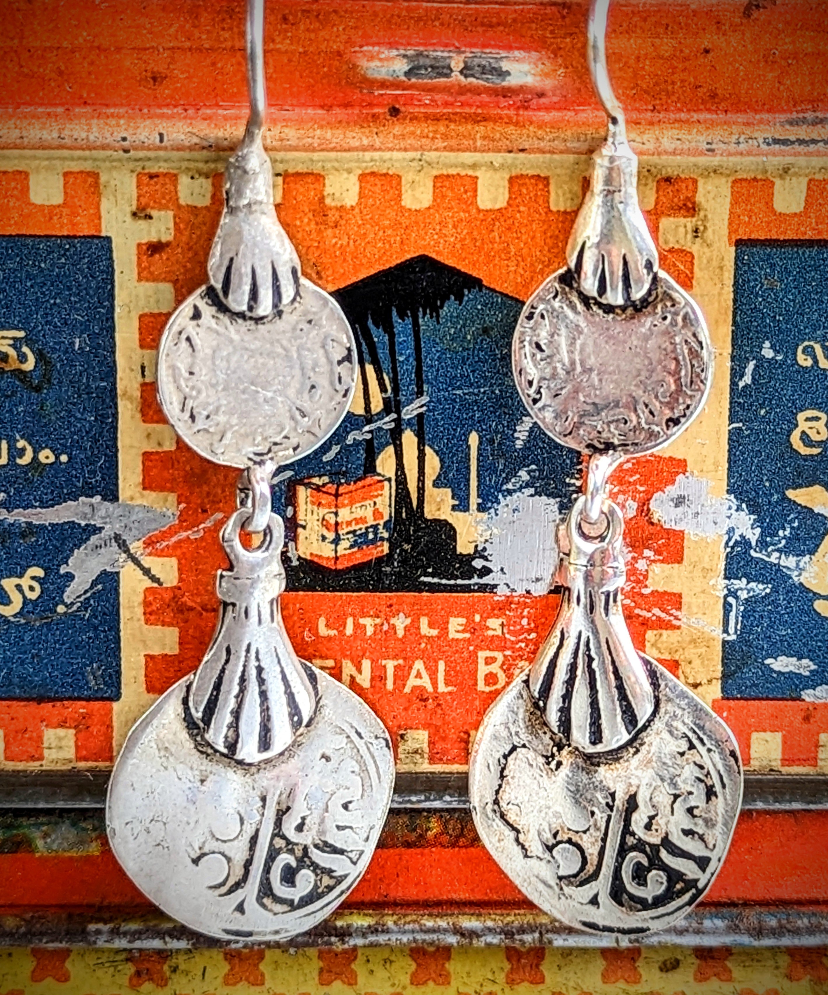 Handmade antique silver Amazigh coin earrings. These are from the Southern Atlas mountains .We love the little hands that are holding the coins!!

These are original pieces so the earring wires are slightly thicker than modern earrings.

Tribal antique silver traditionally has no hallmarks, but all that we sell have an 80-90% content, as these pieces would have been historically made from old melted down jewellery and coins.   