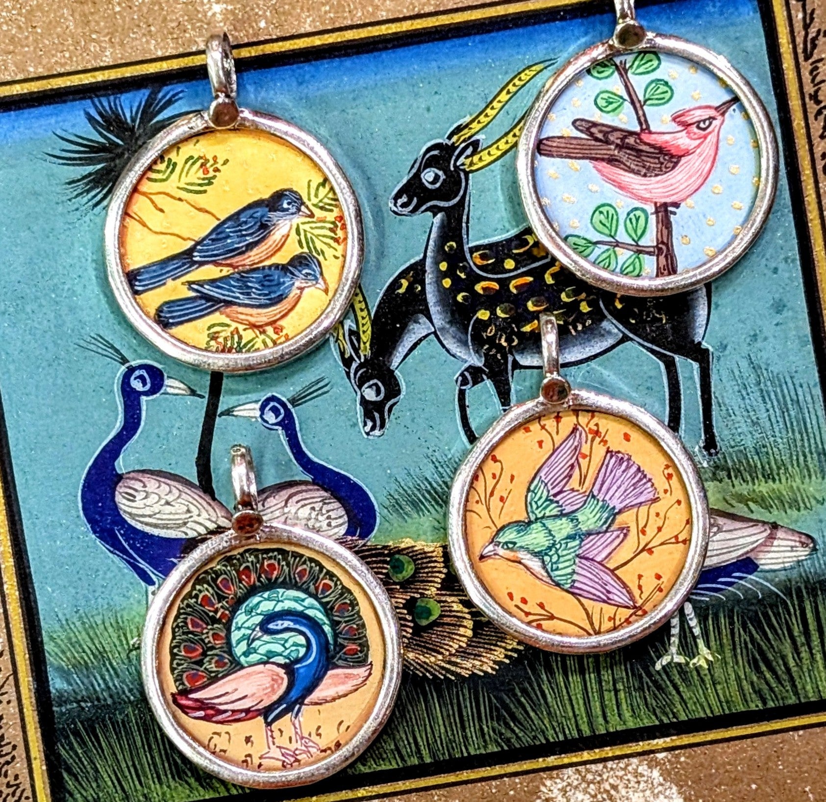 Free flying birds symbolising beauty,  grace, freedom, peace and as messangers between the divine and earth.
Made in Rajasthan, these pendants are crafted from sterling silver, glass and hand painted images on paper. The fine craftsmanship in these paintings is mind blowing, painting with single paint brush bristles!!!

These pendants should be removed when washing/swimming etc as they are in effect framed pieces of art, that although sealed are not water tight! 
Size 25mm diameter and 7mm loop.
