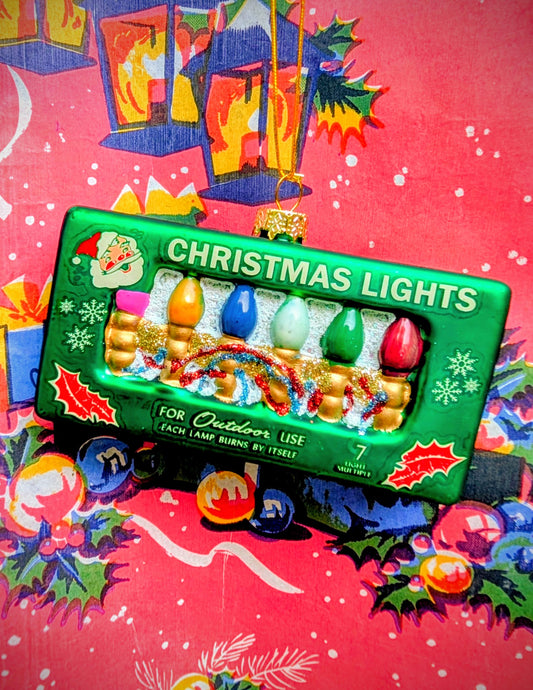 The joy of a box of vintage Xmas lights in a bauble!! Gorgeous, and based on vintage American Christmas advertising artwork 💖

Hand made, painted and glittered for pure joy!!

Size 10cm x 5cm x 2cm

Glass.
Cody Foster & Co 