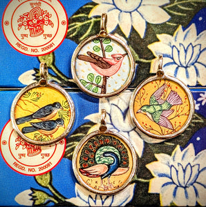 Free flying birds symbolising beauty,  grace, freedom, peace and as messangers between the divine and earth.
Made in Rajasthan, these pendants are crafted from sterling silver, glass and hand painted images on paper. The fine craftsmanship in these paintings is mind blowing, painting with single paint brush bristles!!!

These pendants should be removed when washing/swimming etc as they are in effect framed pieces of art, that although sealed are not water tight! 
Size 25mm diameter and 7mm loop.
