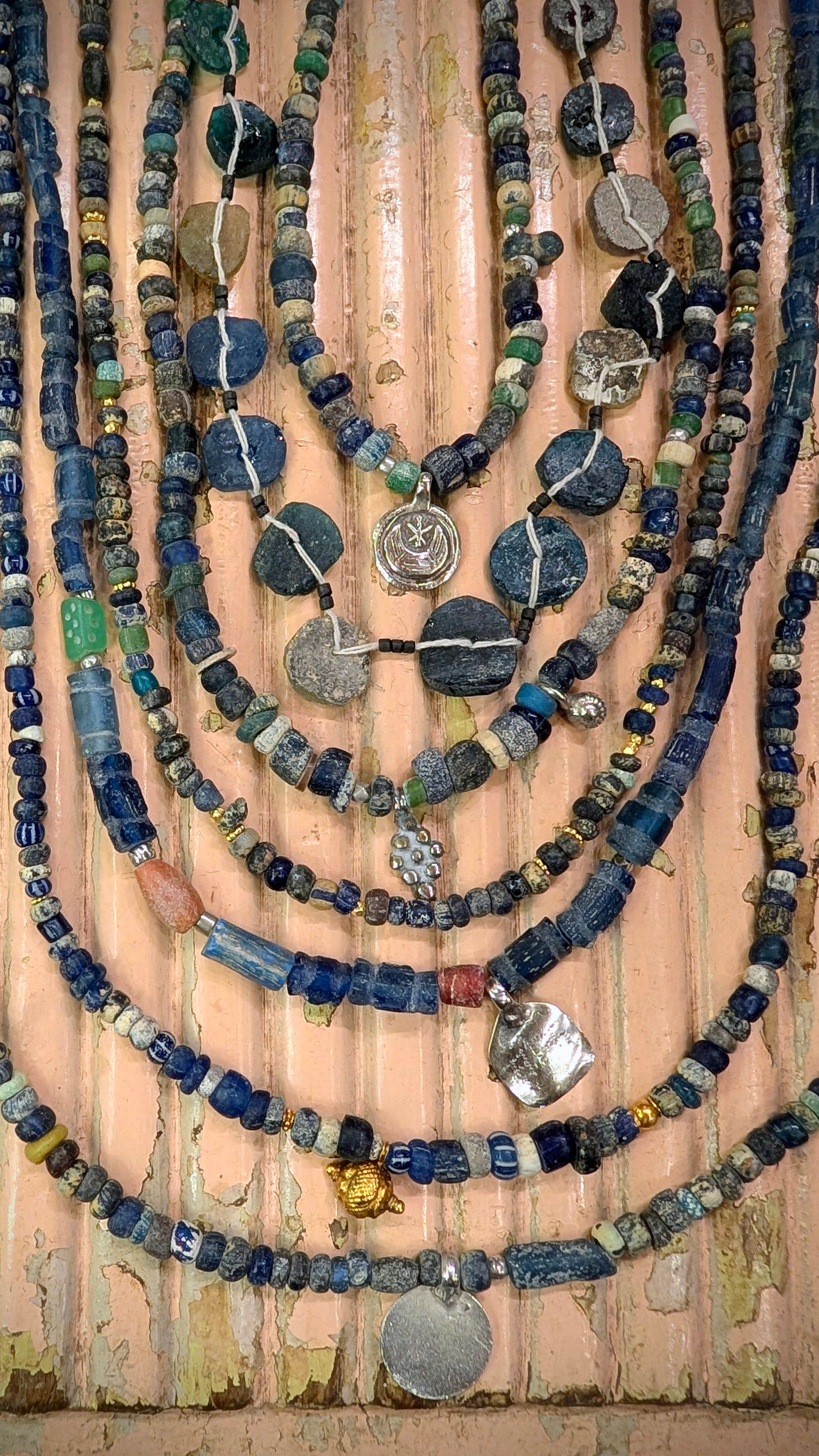 These antique beads are excavated in Mali and Afghanistan, they were traditionally buried under the threshold of the home and places of worship for protection and good luck. Blue glass was highly prized.

The Malian beads are Roman period, and the Afghan ones are typically at least 200-300 years old.

We have threaded them up with antique Saharan and Indian silver amulets and beads too.

The patina on the beads is beautiful, they are aged and frosted by generations of wear and being in the ground like sea g